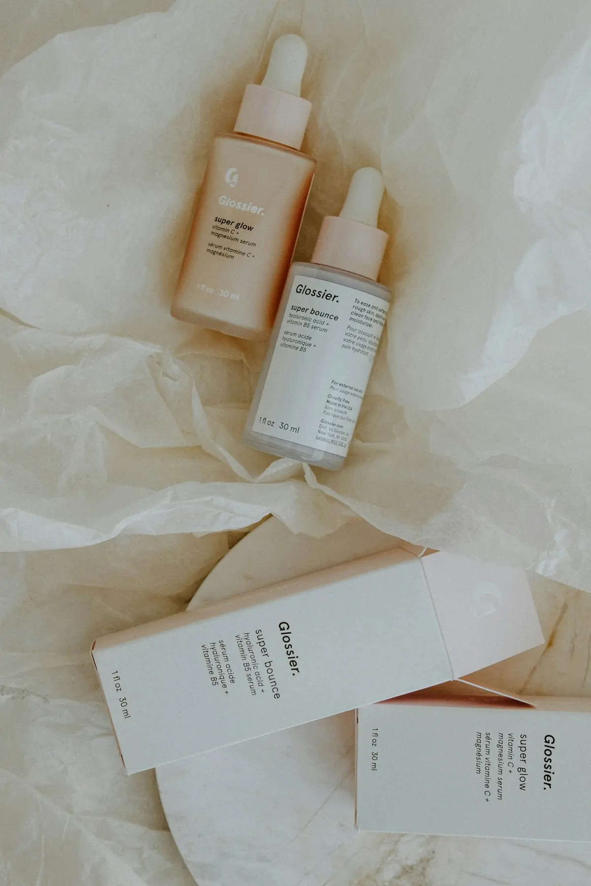 Minimal skincare bottles arranged on soft paper in neutral tones